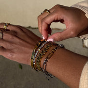 Close-up of hands wearing multiple bracelets with a neutral background